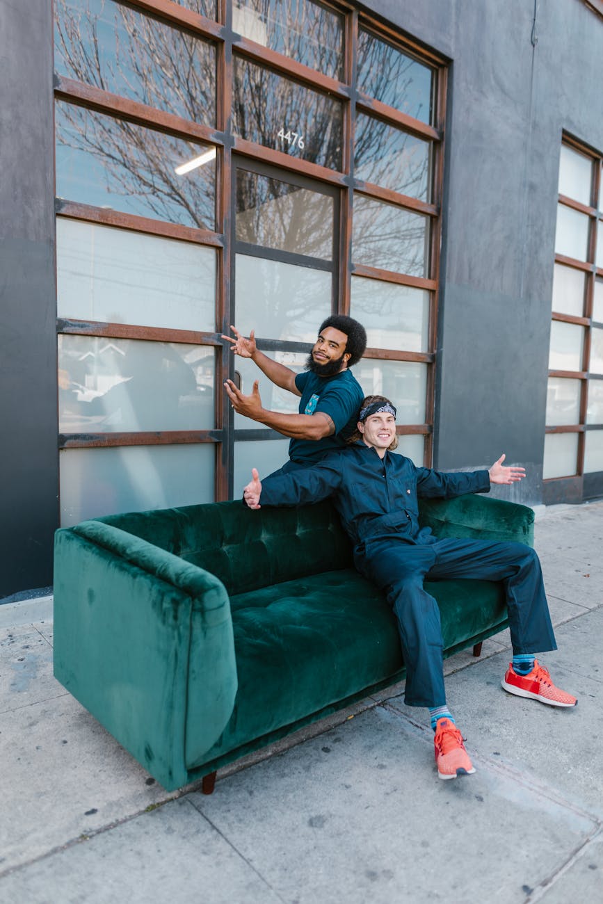 Two movers taking a break on a green sofa outside an urban building, enjoying the day.